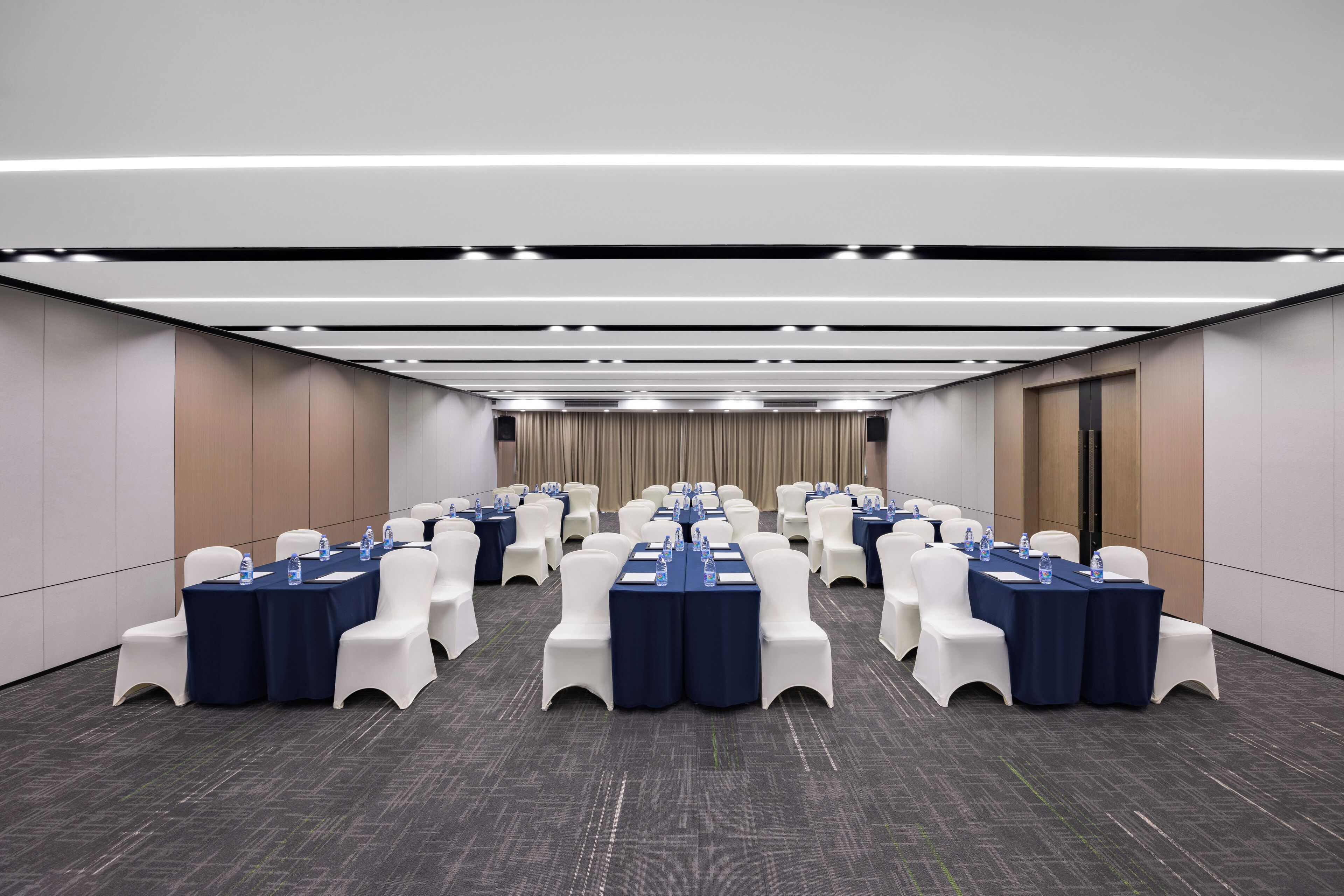 A conference room with rows of tables and chairs, equipped with water bottles and nameplates.