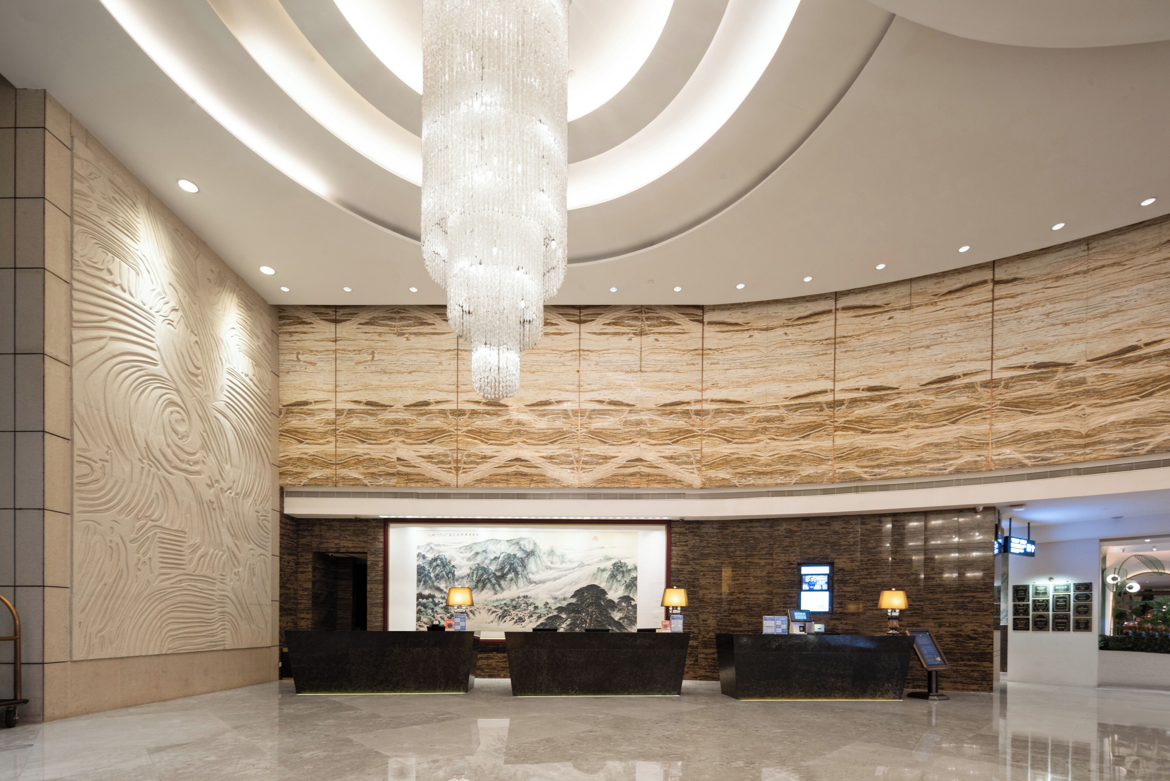 Um hall de hotel moderno com um grande balcão de recepção, um lustre e um mural de parede imponente.