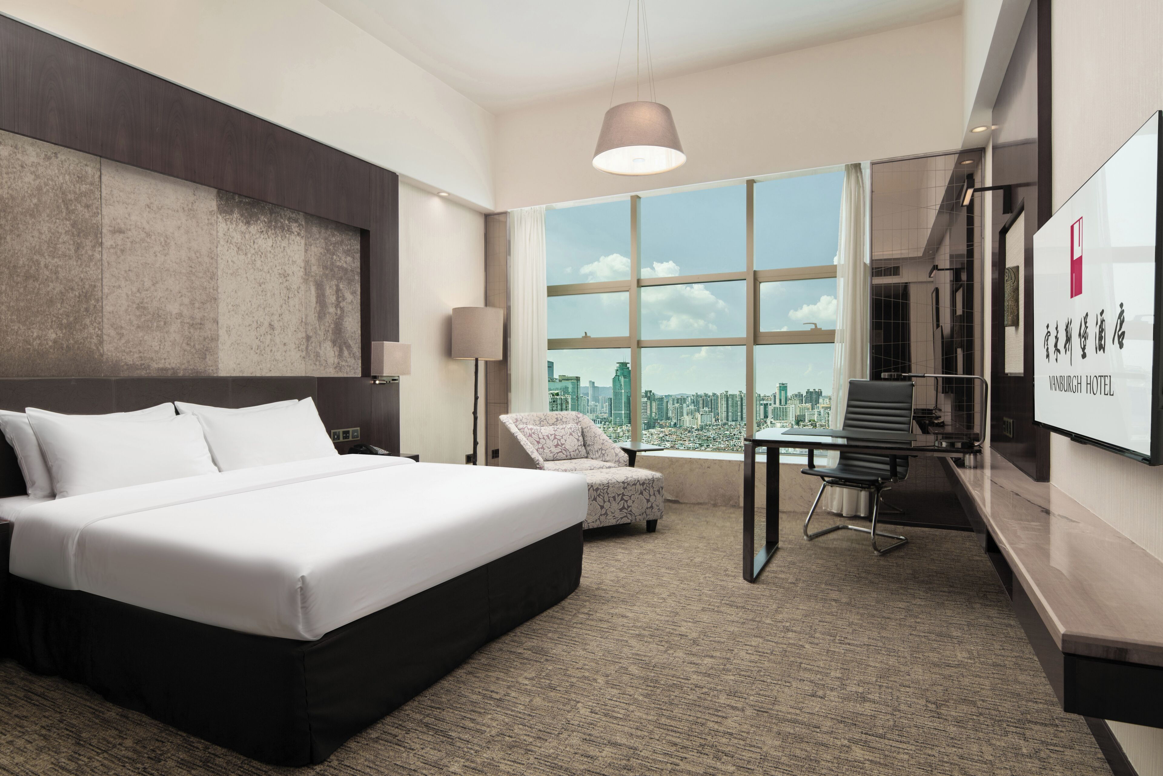 A modern hotel room with a large bed, a desk, a chair, and a city view.