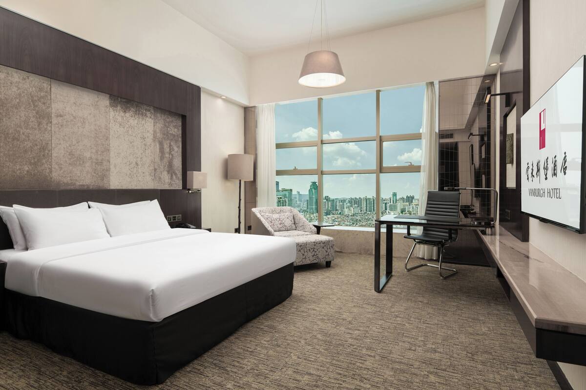 A modern hotel room with a large bed, a desk, and a view of the city.