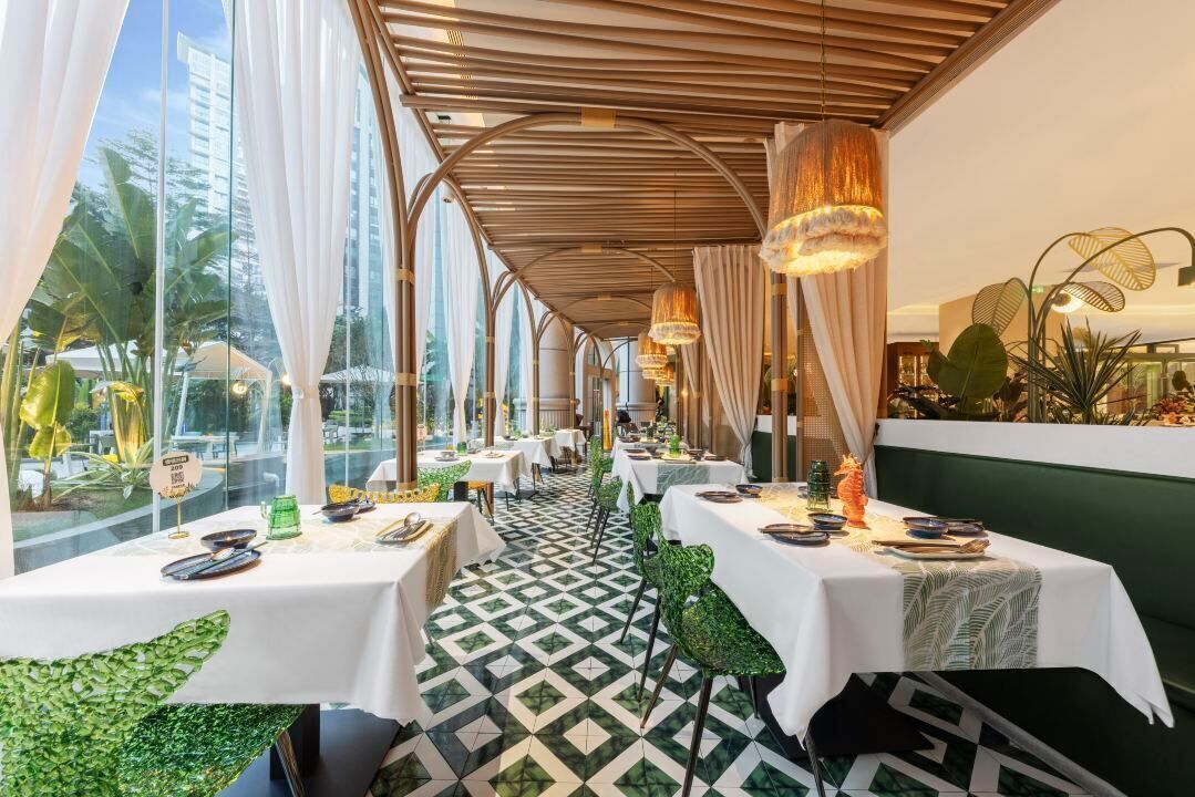 Un restaurante con mesas dispuestas para comer, un suelo estampado y vistas amplias a través de grandes ventanales.
