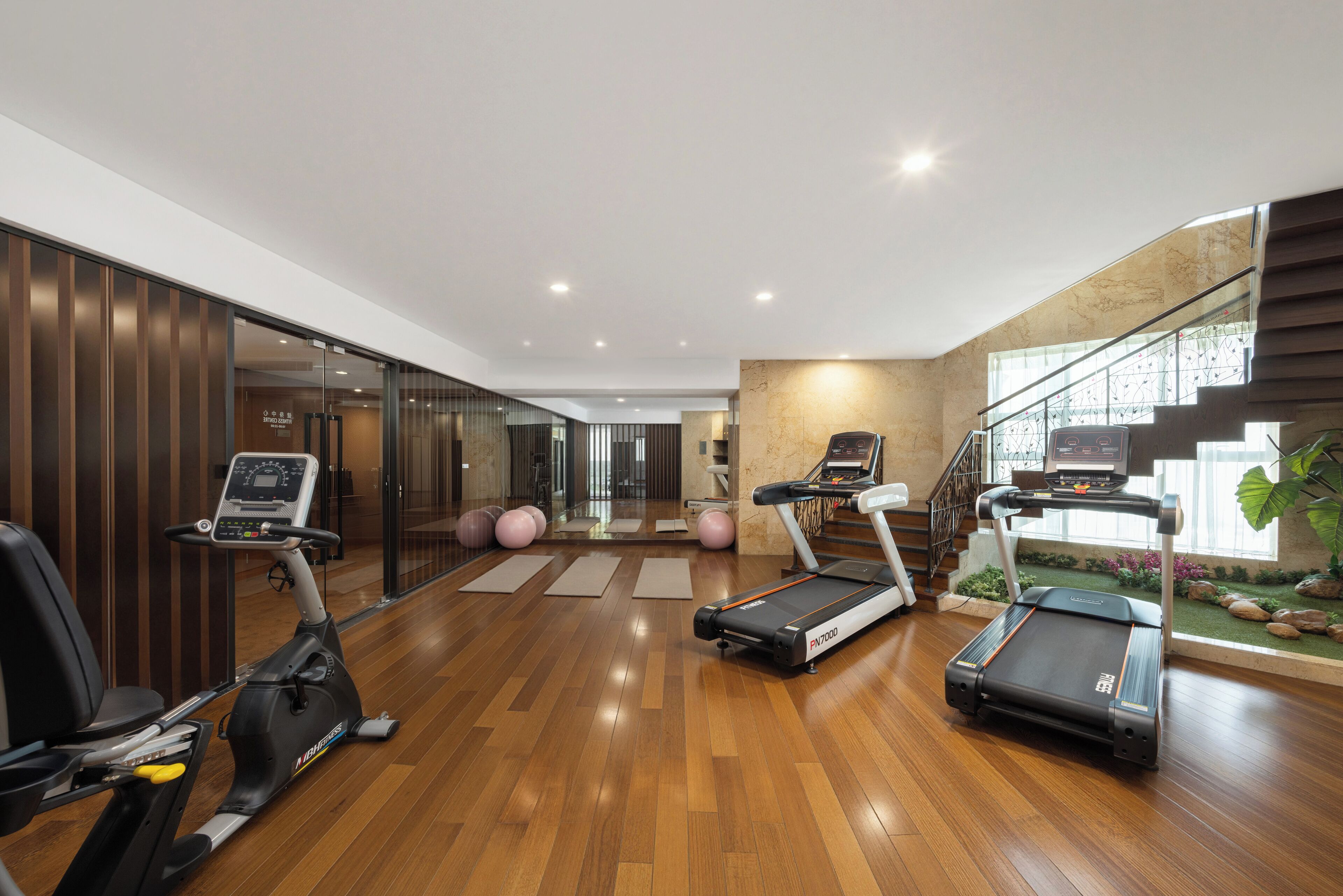 Une salle de sport moderne, équipée de matériel d’exercice, dotée d’un plancher en bois et d’un escalier menant à un niveau supérieur.