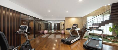 Une salle de sport moderne, équipée de matériel d’exercice, dotée d’un plancher en bois et d’un escalier menant à un niveau supérieur.