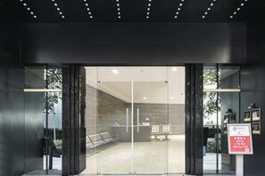 A modern reception area with glass doors, a reception desk, and a waiting area with benches. - Vanburgh Hotel (Guangzhou)