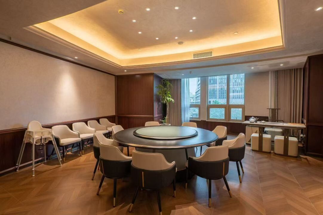 A conference room with a round table, chairs, a small bar area, and large windows.