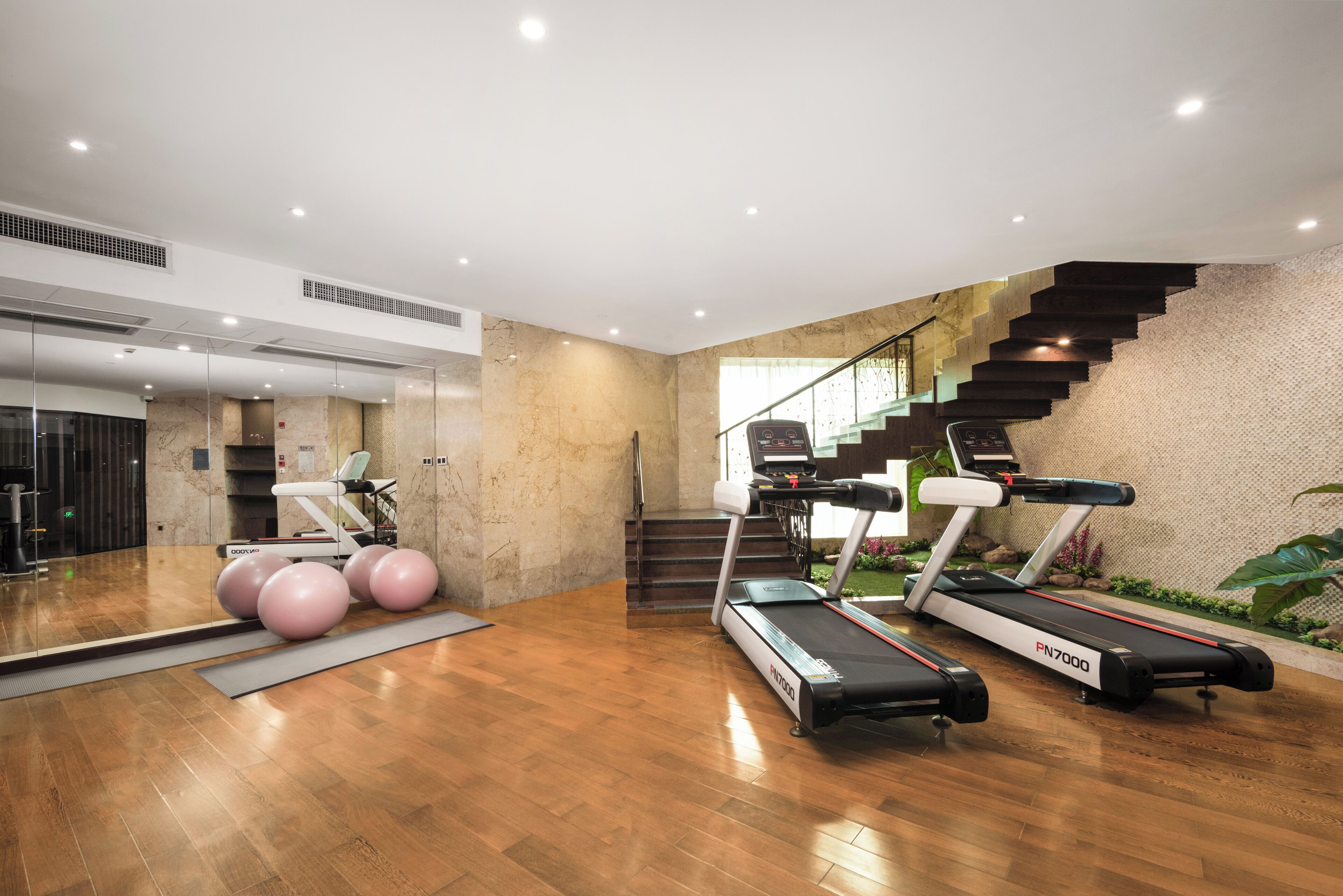 Une salle de sport moderne équipée de tapis de course, de ballons d’exercice et d’un escalier.