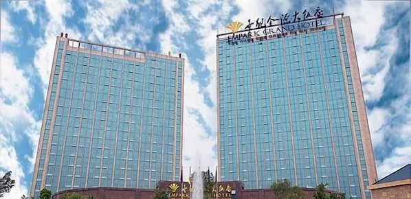 Deux immeubles de grande hauteur aux façades vitrées réfléchissantes, dont l’un porte l’inscription « EMPARK GRAND HOTEL » et l’autre un nom différent, écrit dans un alphabet non latin.