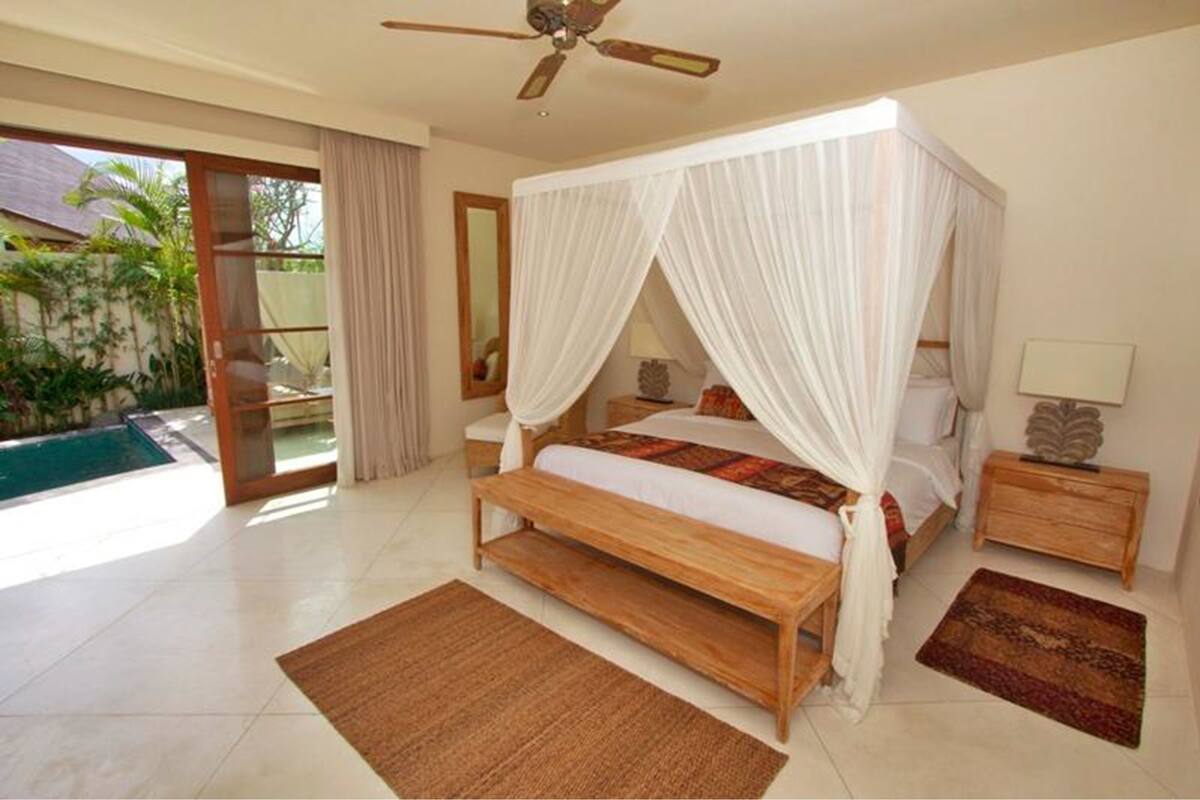 Ein geräumiges Schlafzimmer mit einem hölzernen Bett, einem Deckenventilator und Blick auf einen Swimmingpool.