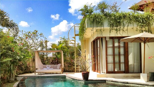 A pool area with a lounge chair, a potted plant, and a building with large windows. - Villa Sahaja (Kerobokan)