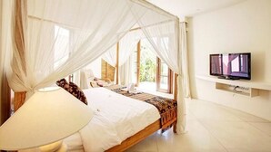 A bedroom with a canopy bed, a television on a shelf, and a view of greenery outside. - Villa Sahaja (Kerobokan)