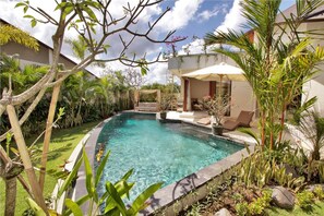 A swimming pool surrounded by lush greenery and a covered seating area.