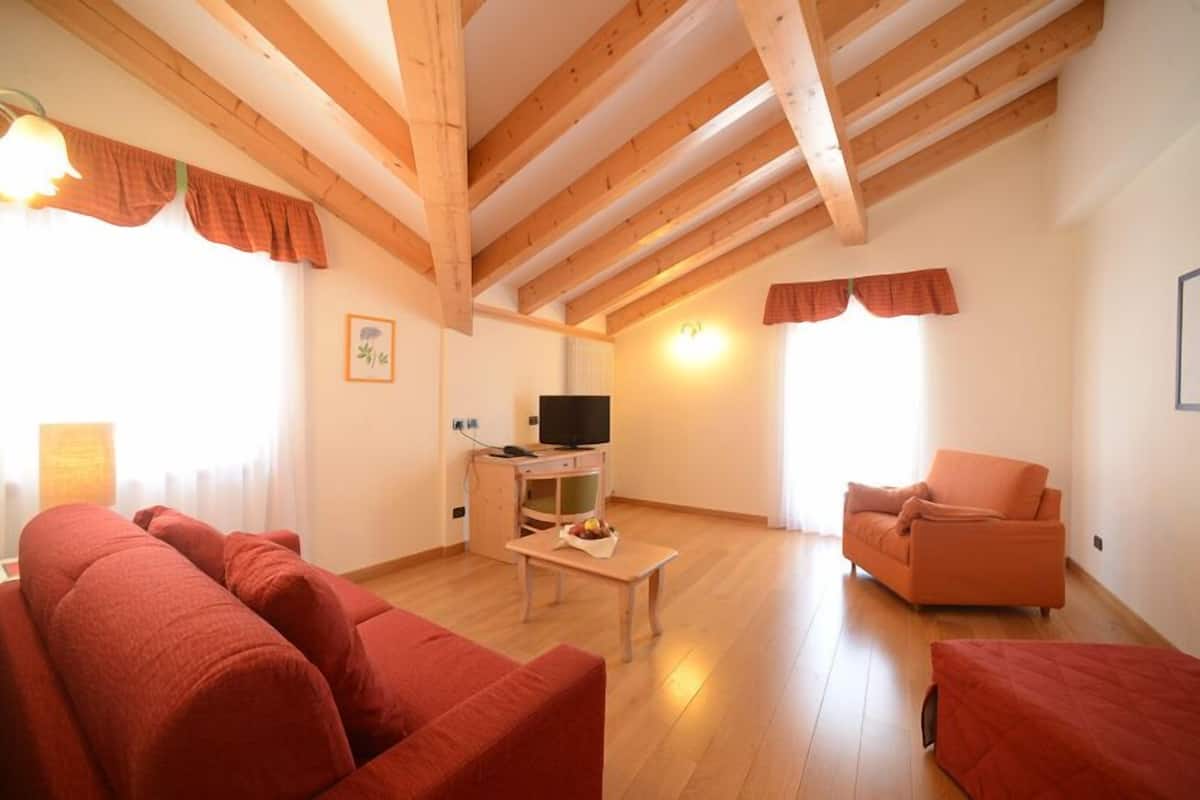 A cozy living room with a wooden ceiling, a television on a stand, a red sofa, and a matching armchair.