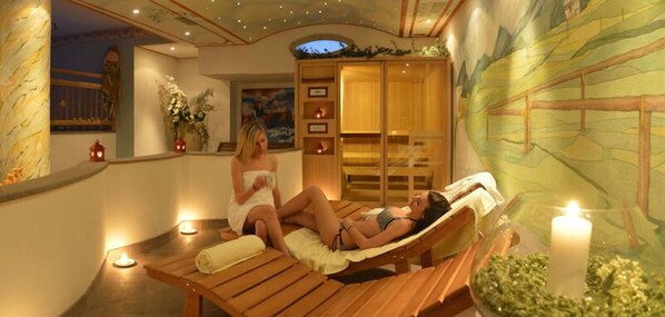 A spa room with wooden loungers, a massage table, and a mural on the wall. - Hotel Paganella Gourmet & Relax (Fai della Paganella)