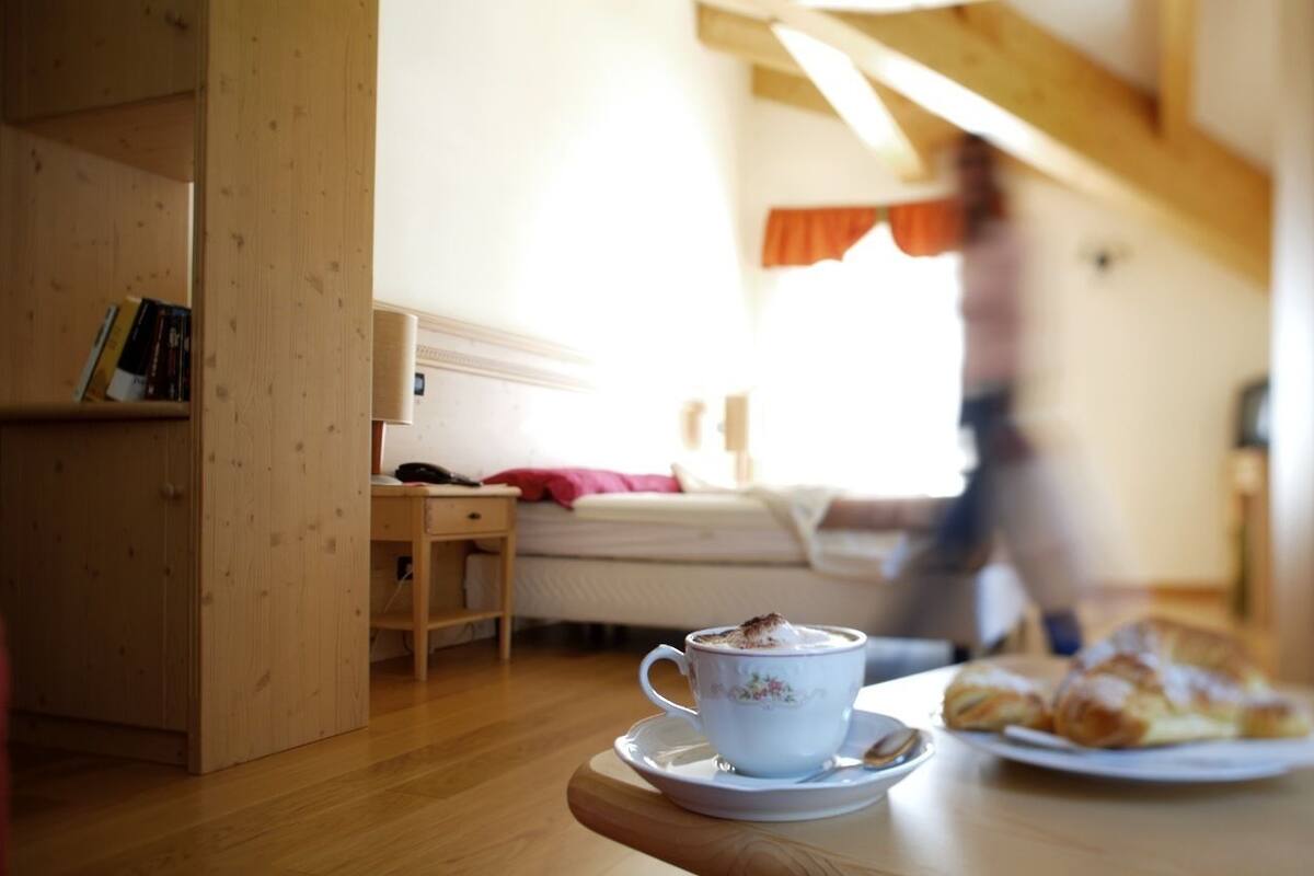 A cozy room with a wooden bookshelf, a bed with a red blanket, a cup of coffee on a table, and a plate of pastries.