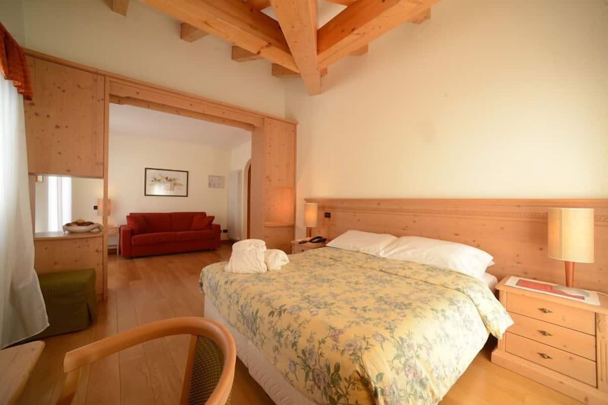 A bedroom with a wooden headboard, a floral bedspread, a red sofa, and a wooden nightstand with a lamp.