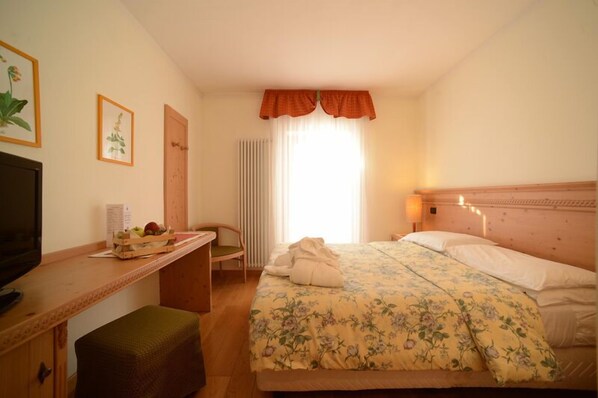 A hotel room with a bed, a desk, a chair, a television, and a window with curtains. - Hotel Paganella Gourmet & Relax (Fai della Paganella)