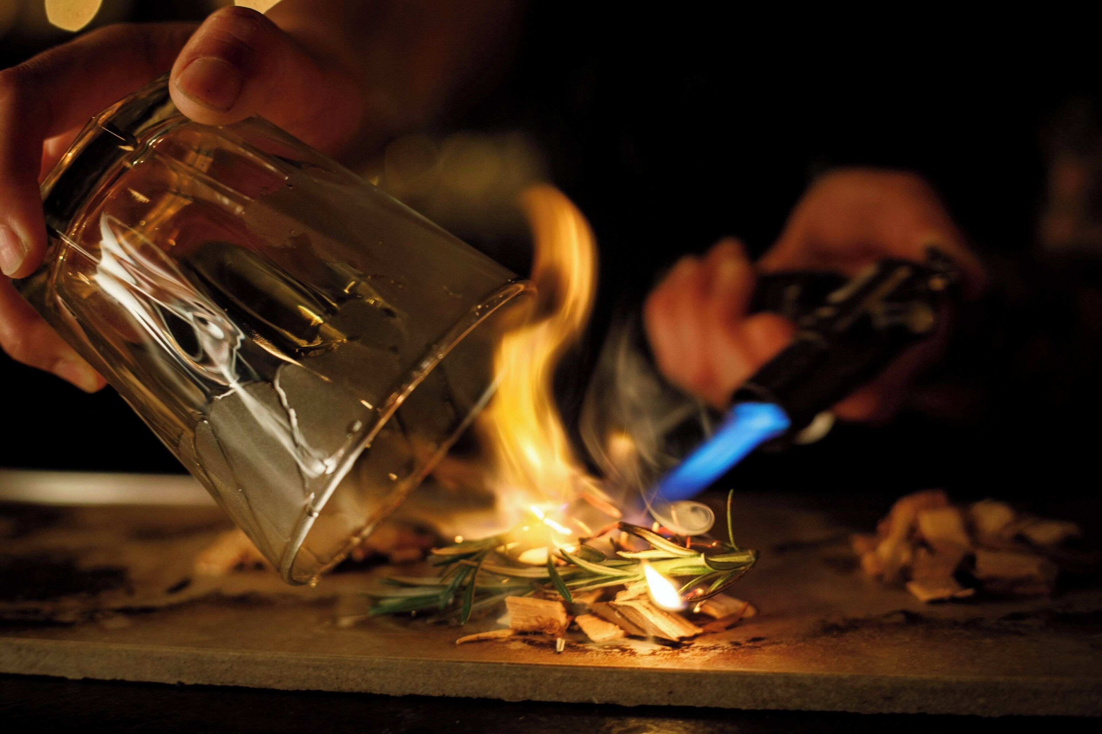 A person holding a glass and lighting a candle with a lighter.