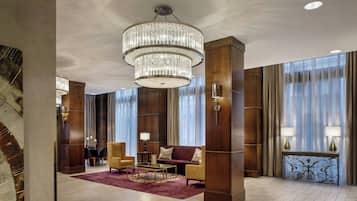 A spacious lobby with a large chandelier, plush seating, and a wooden reception desk.