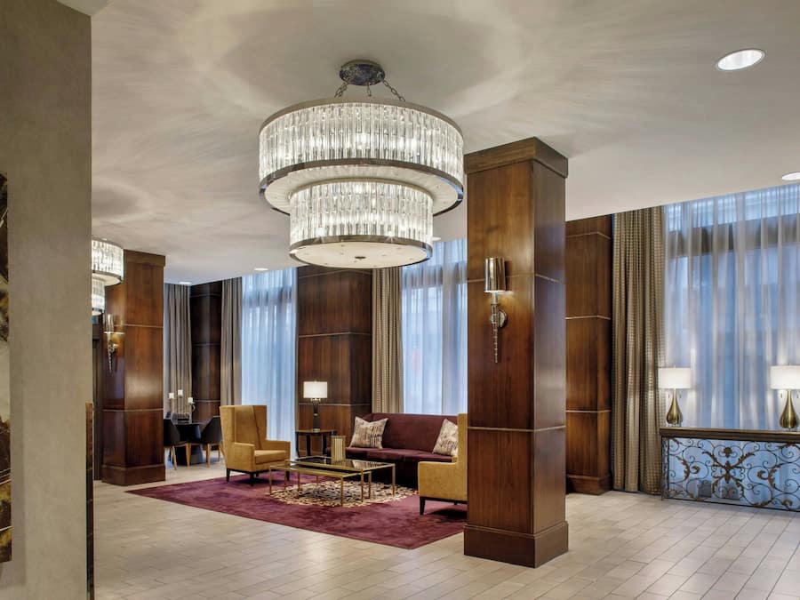 Un hall d’entrée spacieux, agrémenté d’un grand lustre, de fauteuils confortables et d’un comptoir d’accueil en bois.