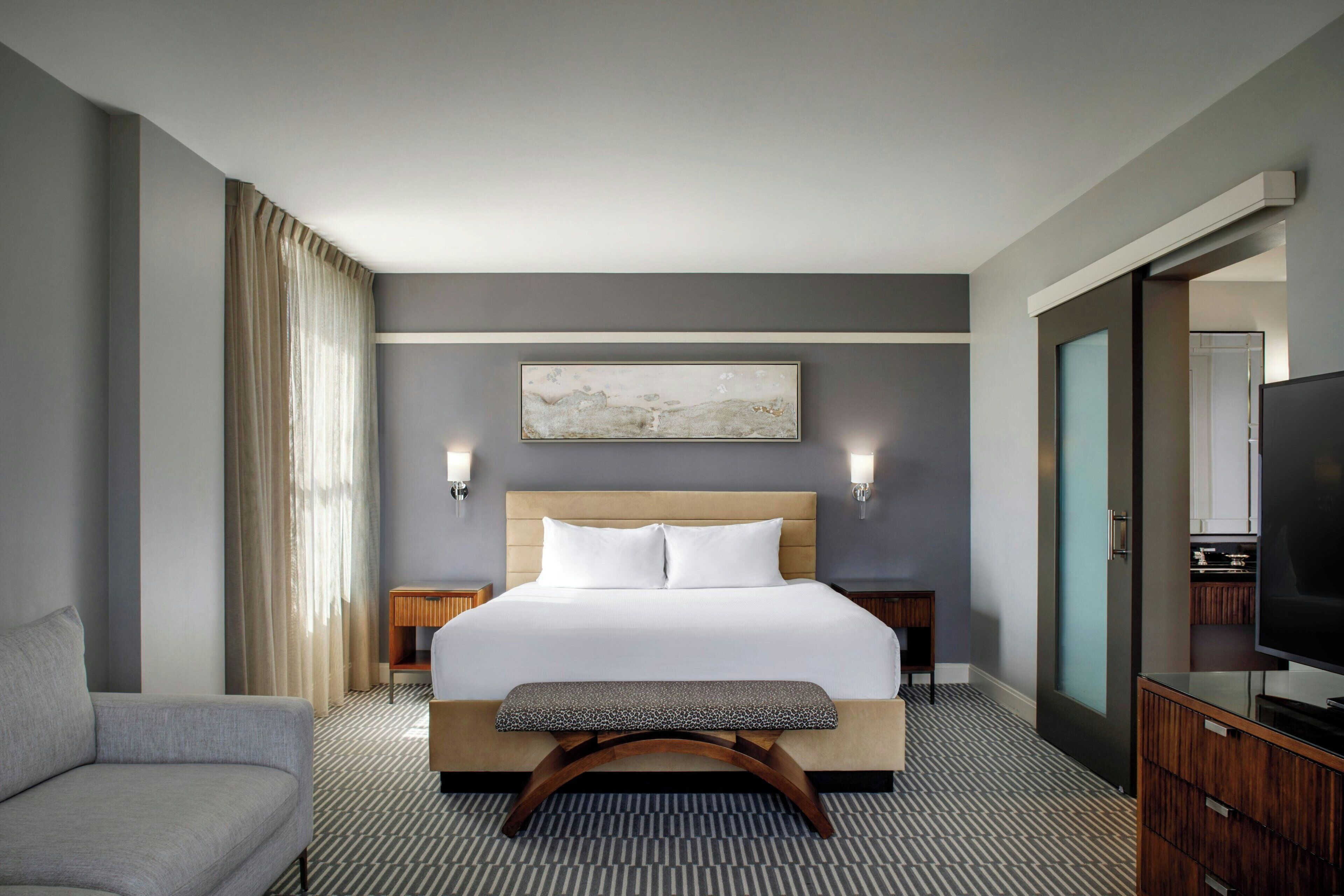 Habitación de hotel con una cama grande, un sofá, un televisor y un cuadro en la pared.