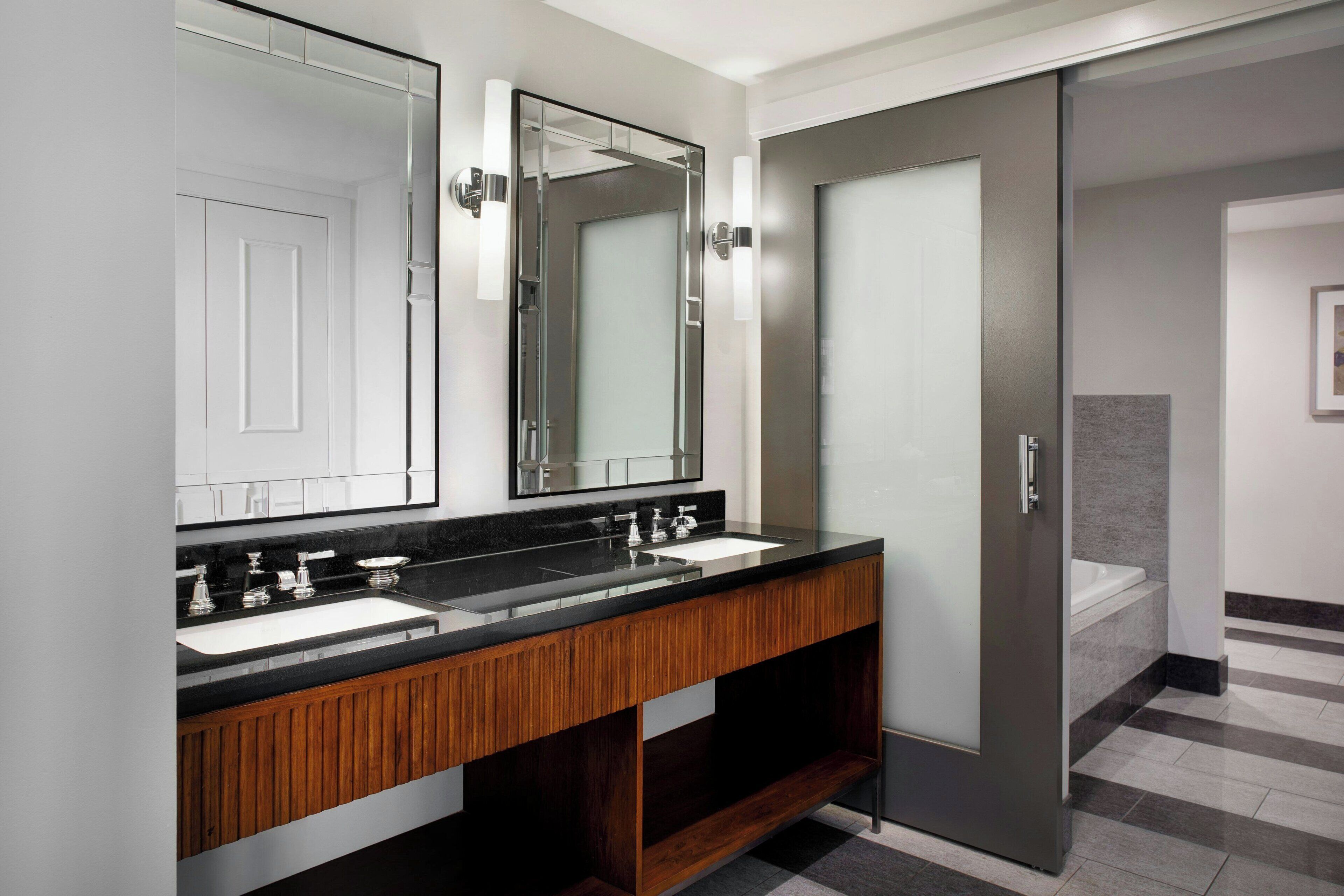 A modern bathroom with two sinks, a large mirror, and a sliding door.