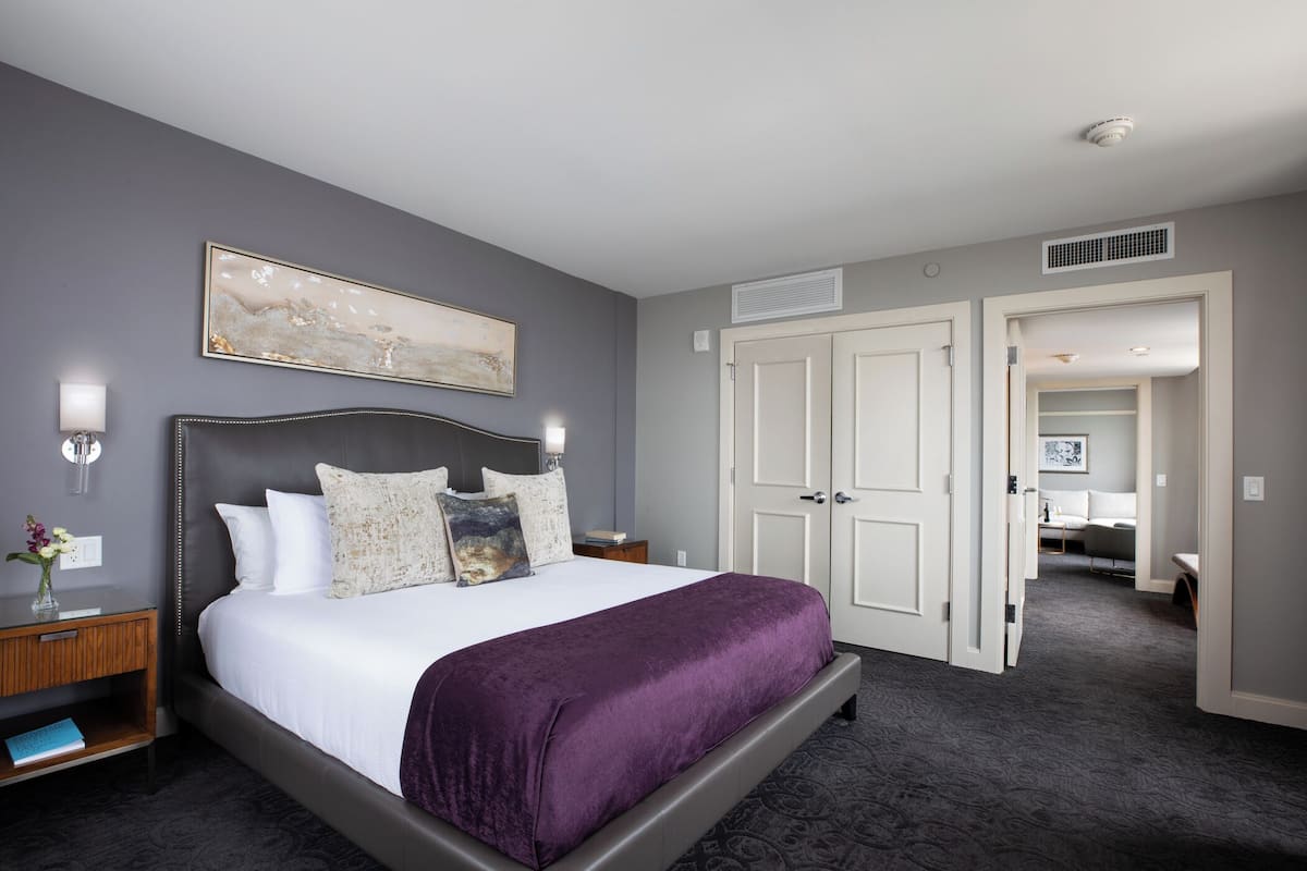 Una habitación de hotel moderna con una cama grande, una mesita de noche, una lámpara de pared y una puerta que da al baño.