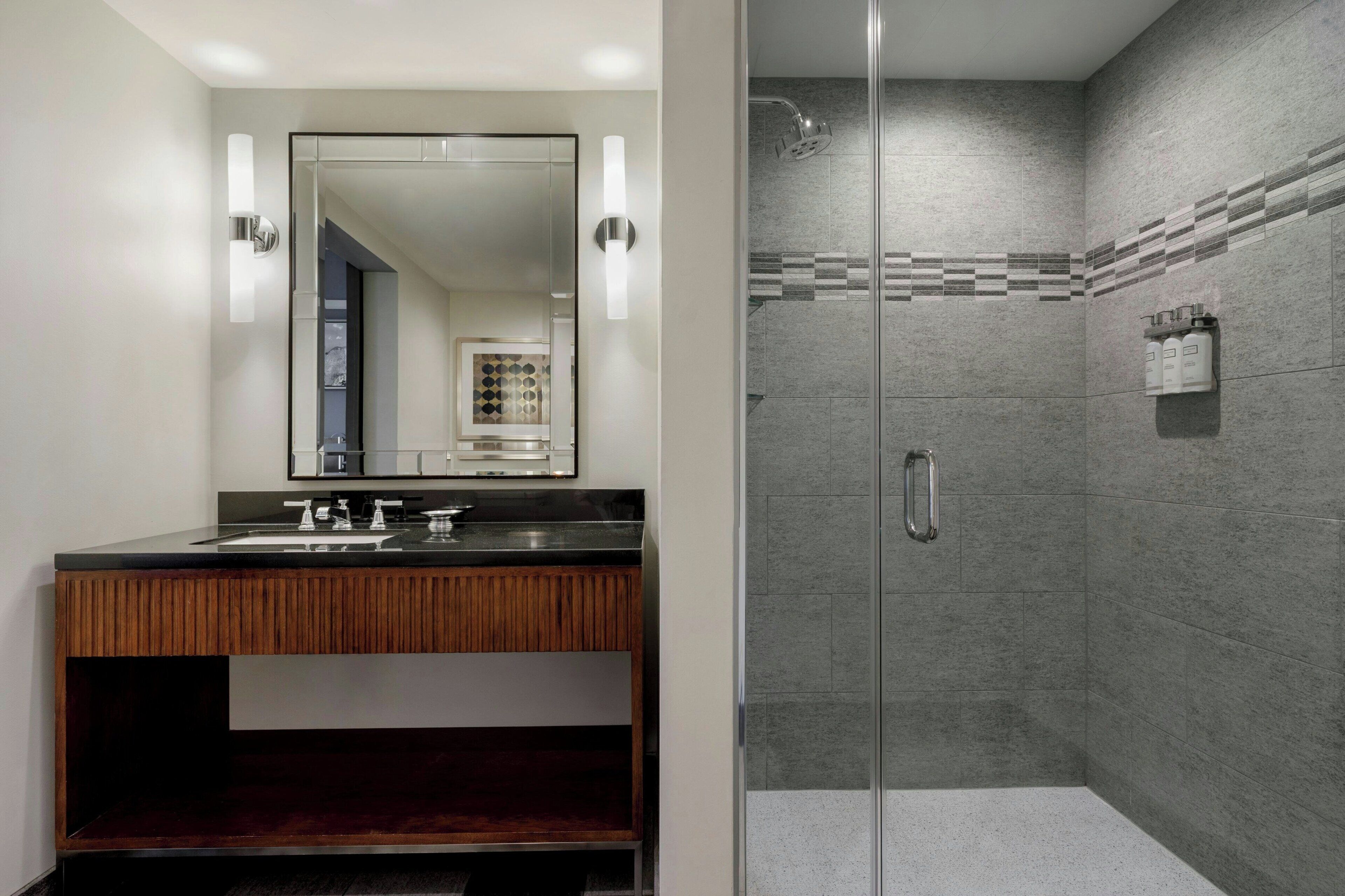Une salle de bain moderne avec un meuble-lavabo en bois, un grand miroir et une douche séparée par des parois en verre.