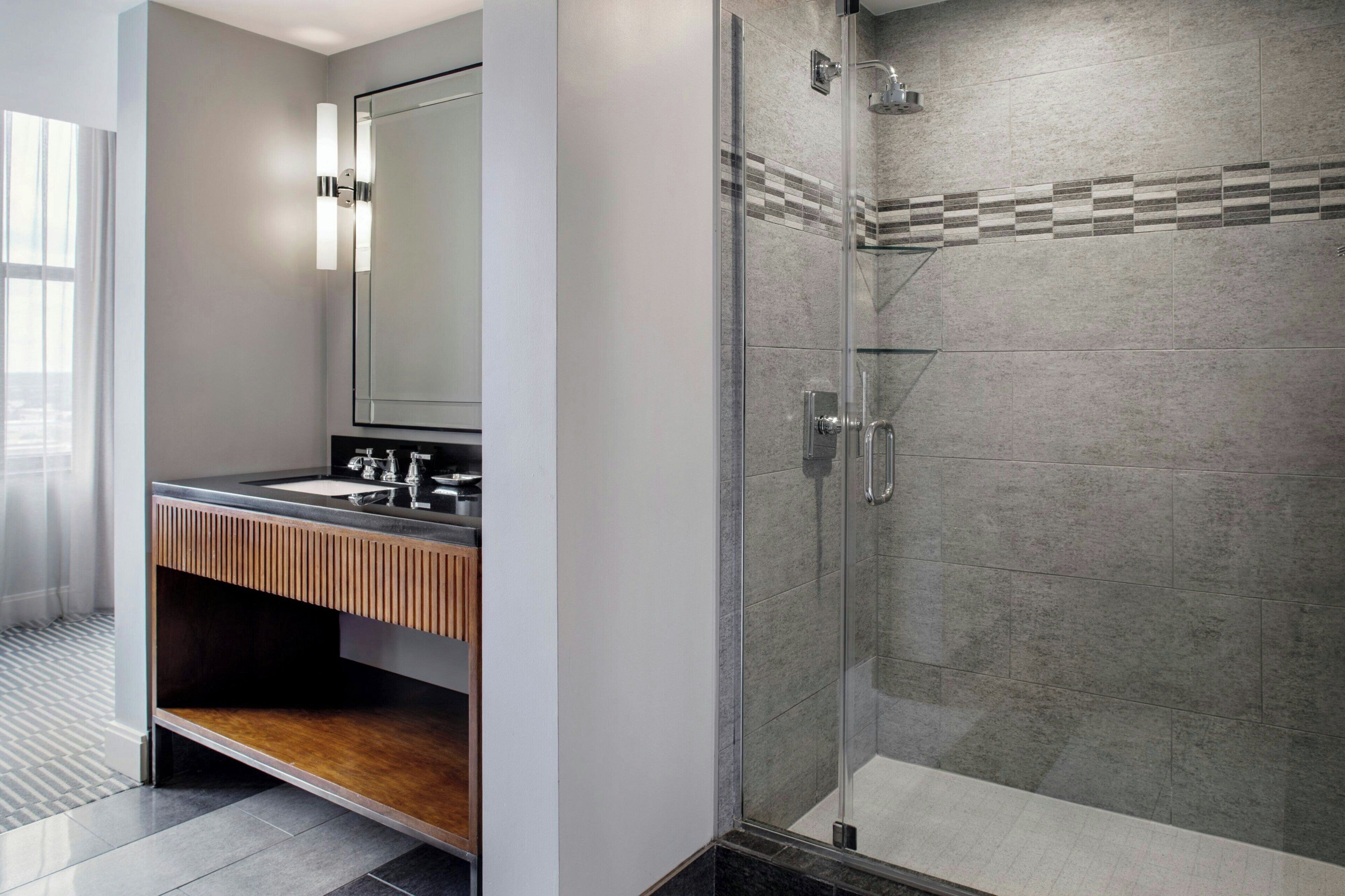 Un bagno moderno con cabina doccia in vetro, mobile lavabo in legno e uno specchio grande.