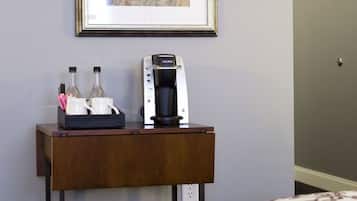 A hotel room with a framed map on the wall, a coffee maker, and a small table with bottles and a mug.