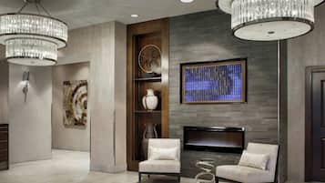A modern lobby with two chandeliers, a fireplace, a TV mounted on the wall, and two armchairs.