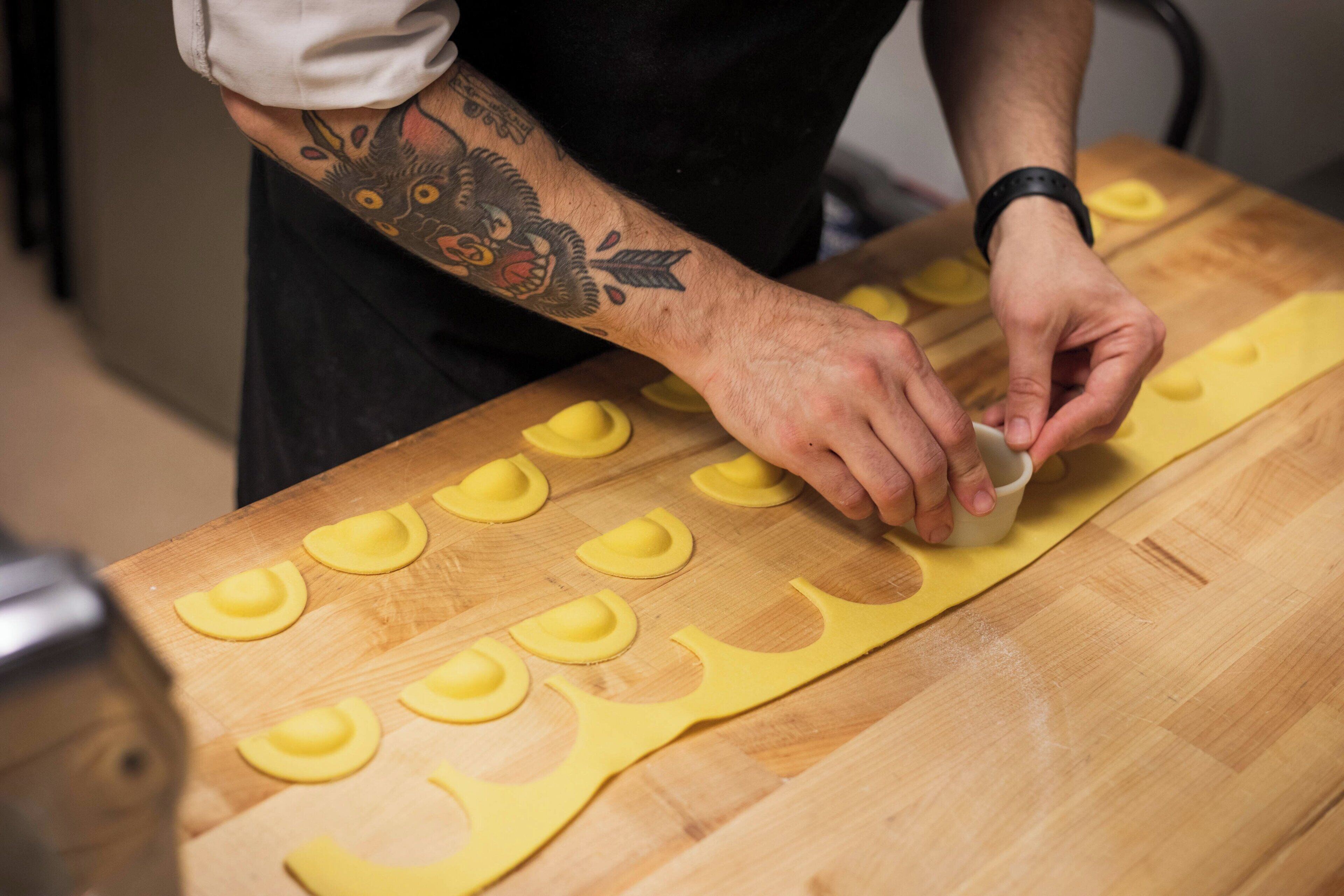 Une personne prépare des aliments sur une table en bois, à côté d'une pâte jaune et d'un couteau.