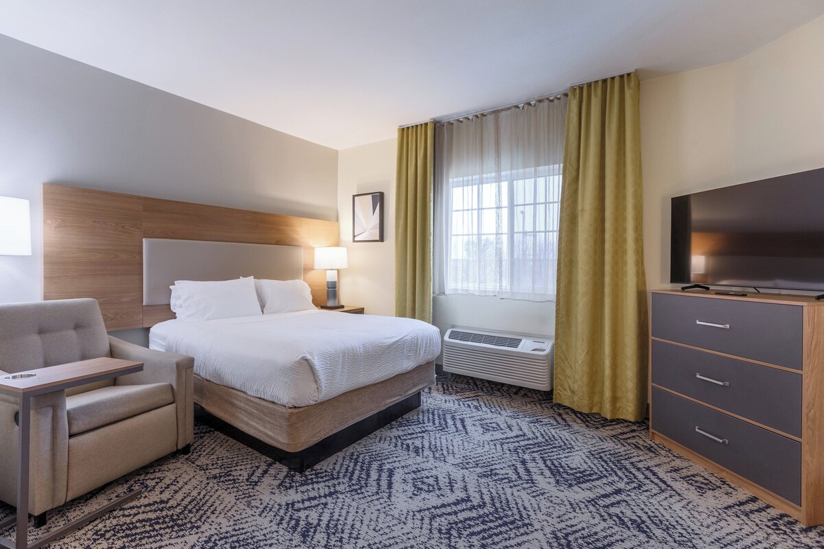 A hotel room with a bed, a desk, a chair, a TV, and a dresser.