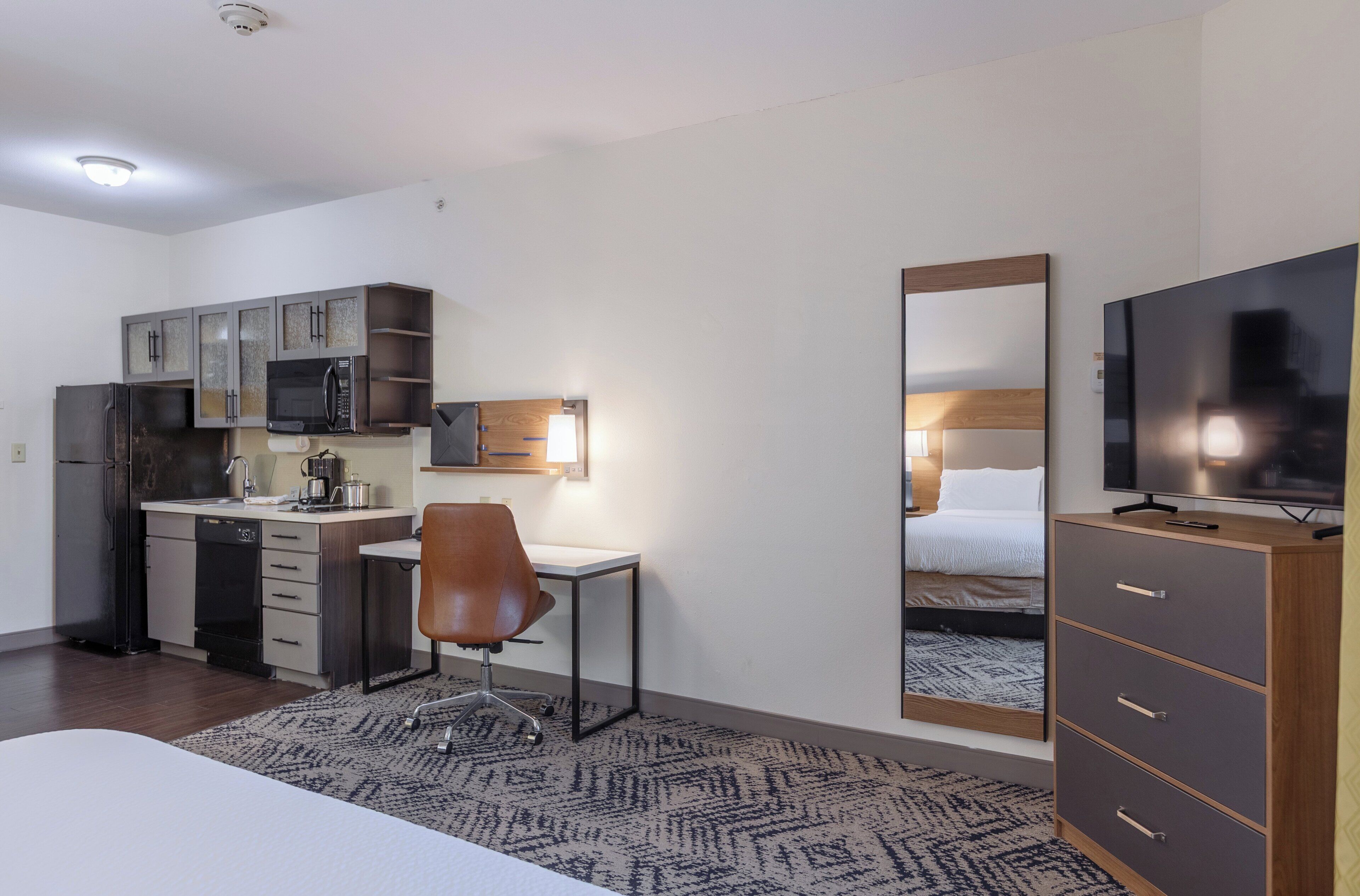 A compact hotel room with a kitchenette, a single bed, a TV, and a mirror.