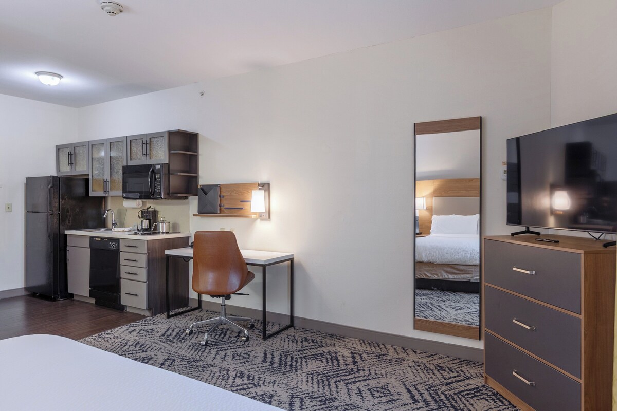 A compact hotel room with a kitchenette, a single bed, a TV, and a mirror.