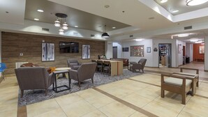 Un hall d’entrée spacieux au design moderne, agrémenté d’un mur d’accent en bois, d’un espace détente avec des canapés et des fauteuils, d’une petite table et d’un comptoir de réception.