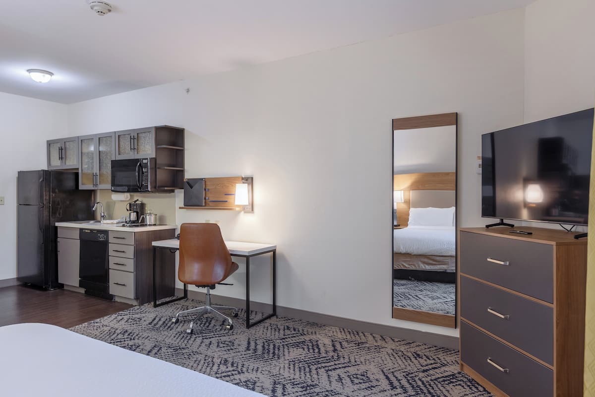 Ein kleines Hotelzimmer mit Küchenzeile, einem Einzelbett, einem Fernseher und einem Spiegel.