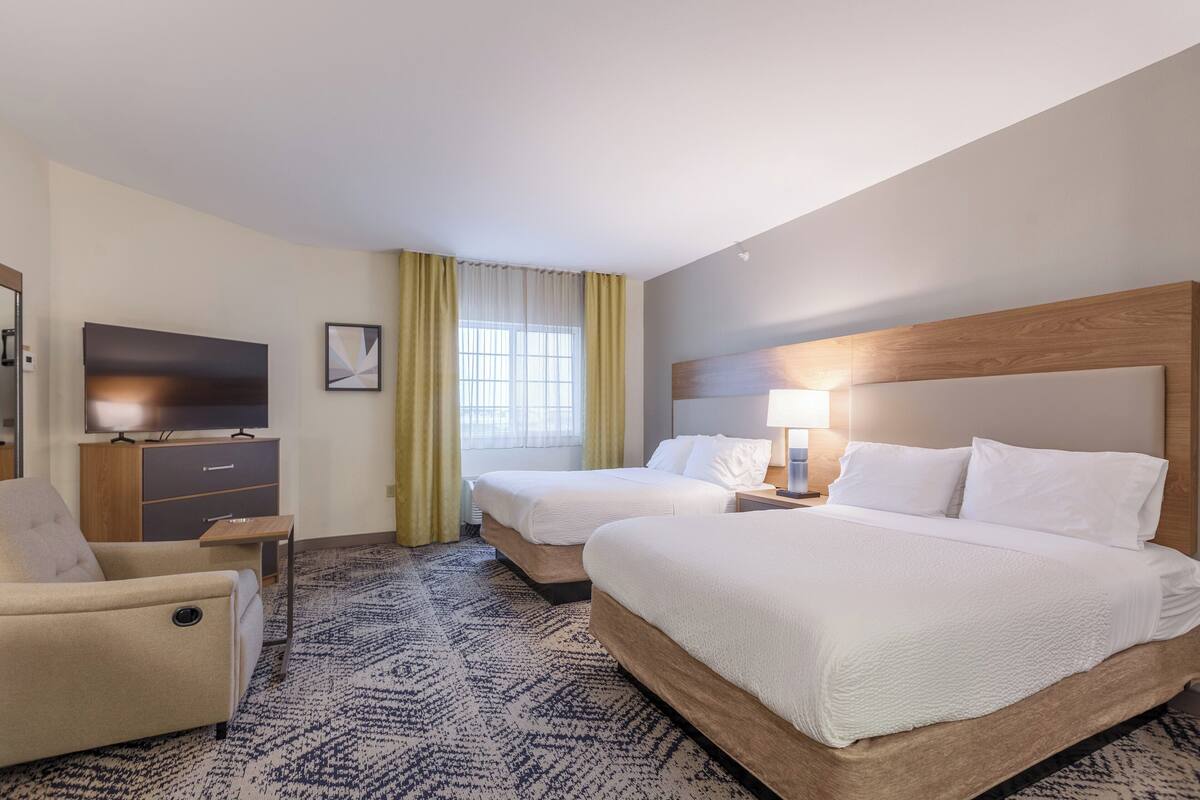 Ein Hotelzimmer mit zwei Betten, einem Fernseher, einem Schreibtisch und einem Sessel.