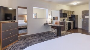 Une chambre d’hôtel équipée d’un lit, d’un bureau, d’une chaise, d’une télévision, d’un four à micro-ondes, d’un réfrigérateur et d’un coin cuisine.