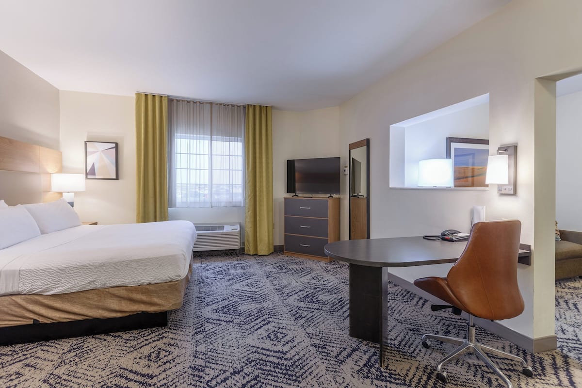 Ein Hotelzimmer mit Bett, Schreibtisch, Stuhl, Fernseher und einem fenster mit Vorhängen.