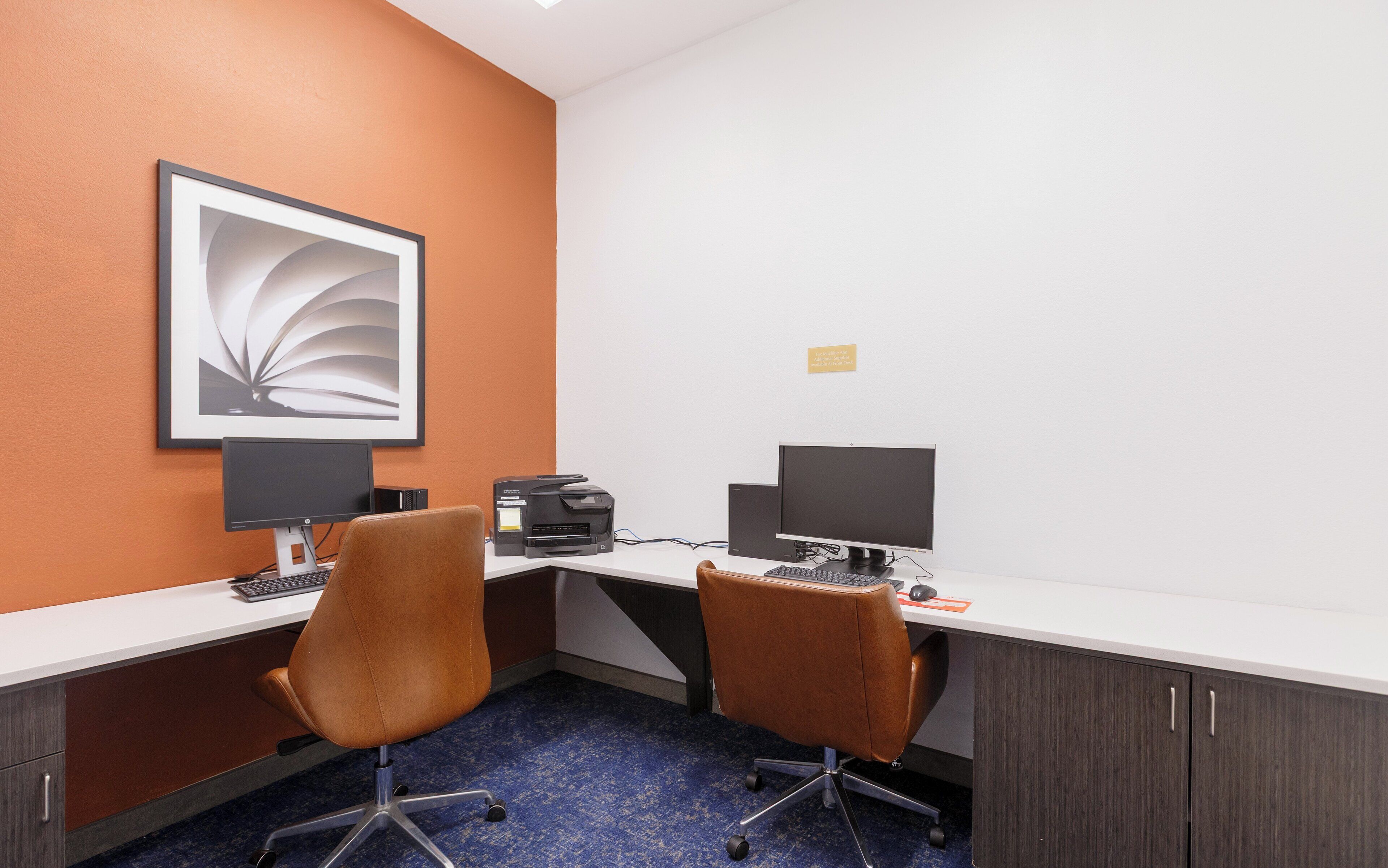 Habitación de hotel con dos escritorios, cada uno con una computadora y teclado, y una obra de arte enmarcada en la pared.