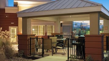 A covered outdoor seating area with tables and chairs, a pathway leading to the entrance, and a view of the mountains in the background.