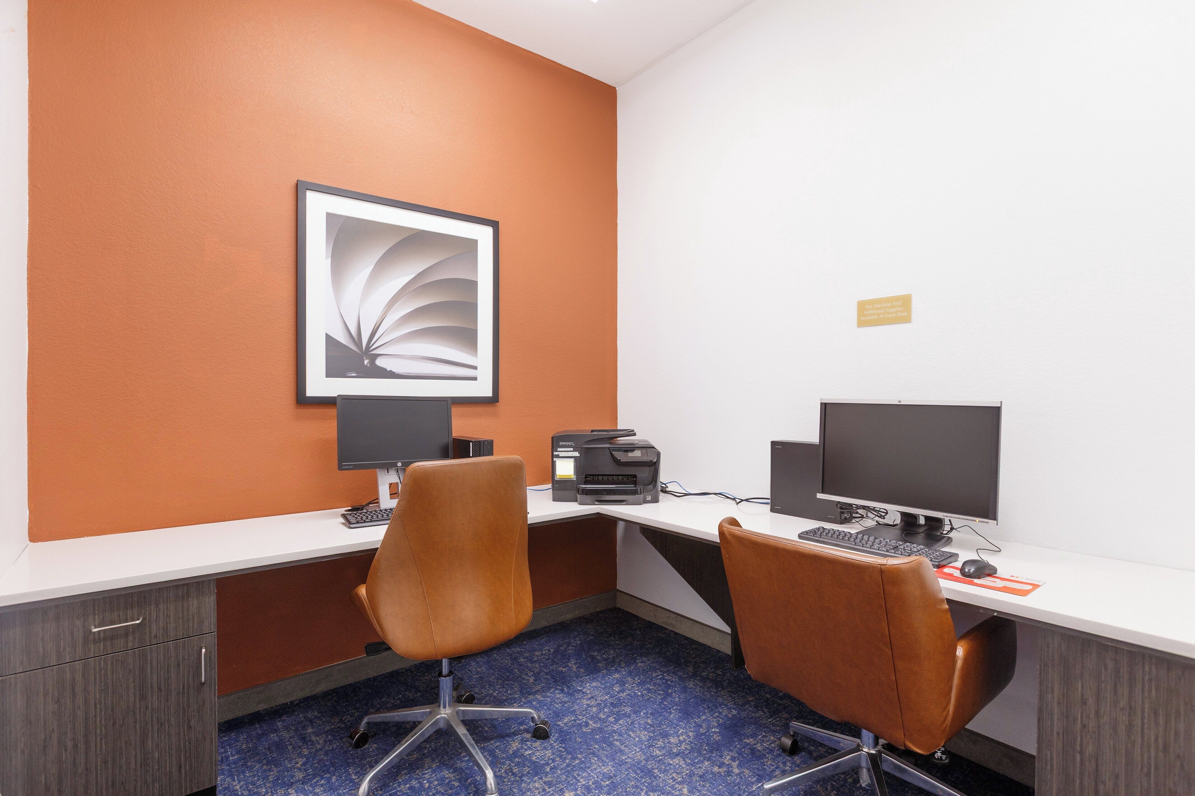 Habitación de hotel con dos escritorios, cada uno con una computadora, teclado, impresora y una silla.