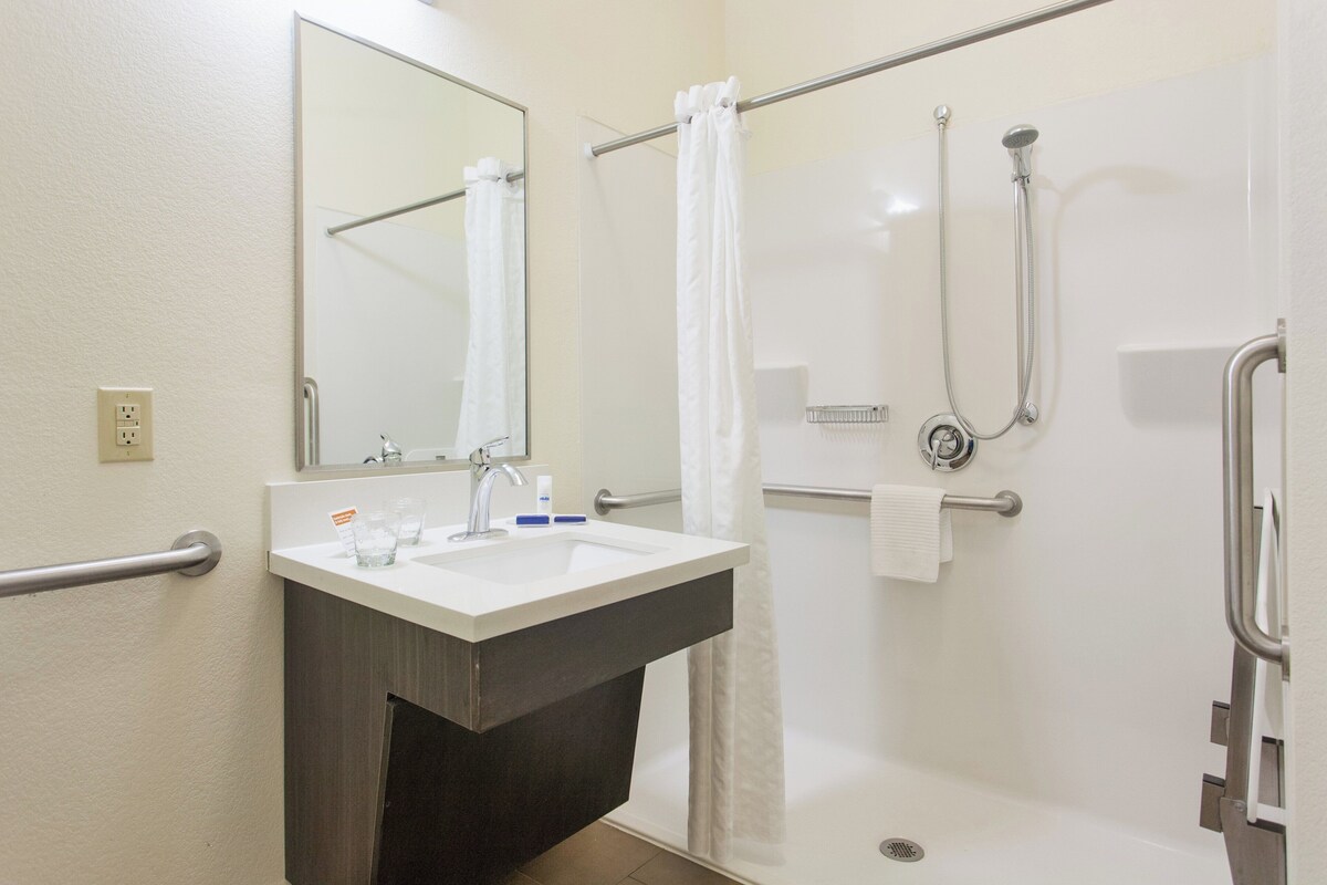 A bathroom with a sink, mirror, shower, and grab bars.