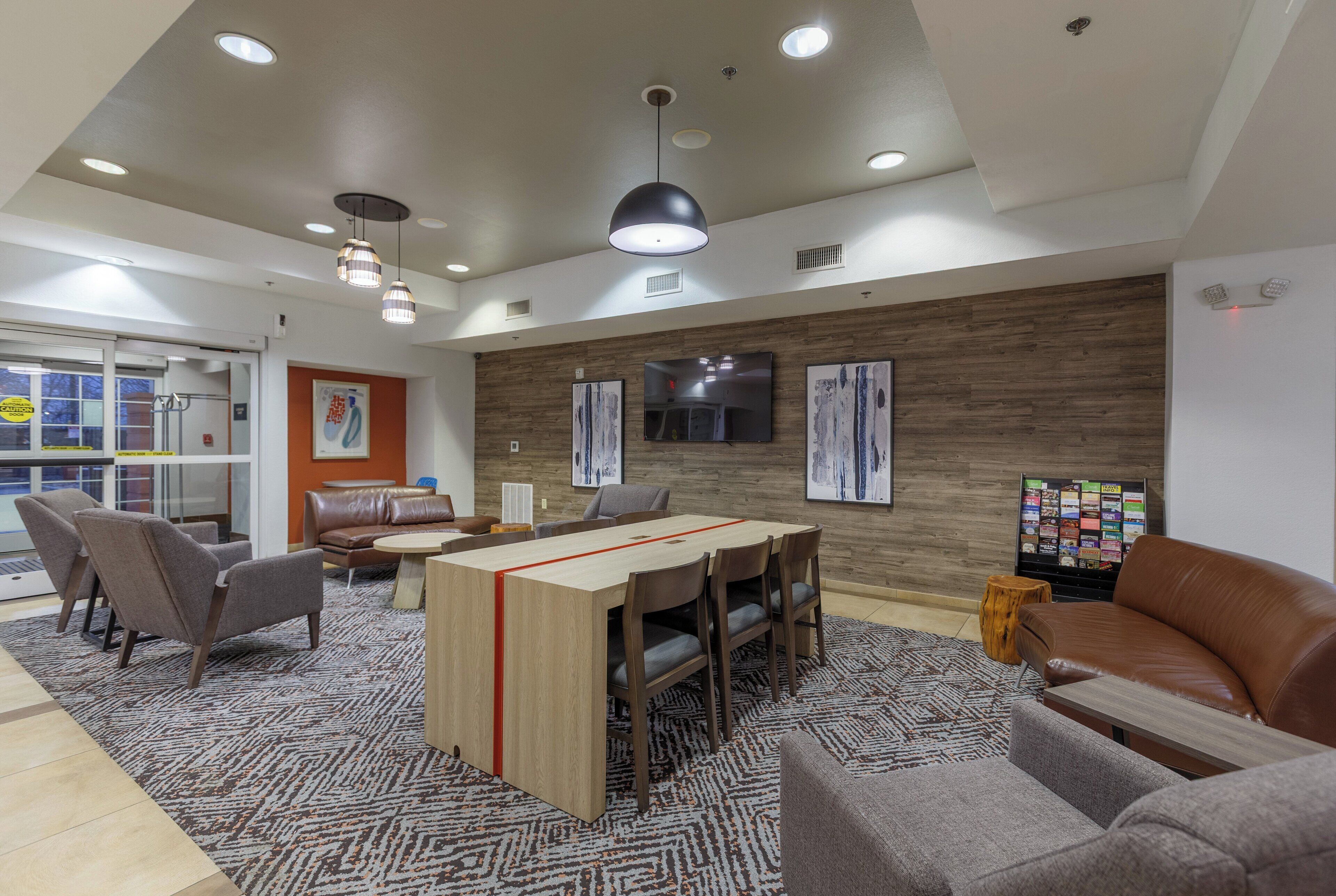 Un intérieur moderne avec un mur en bois, un téléviseur et un coin salon comprenant un canapé en cuir marron et des fauteuils gris.