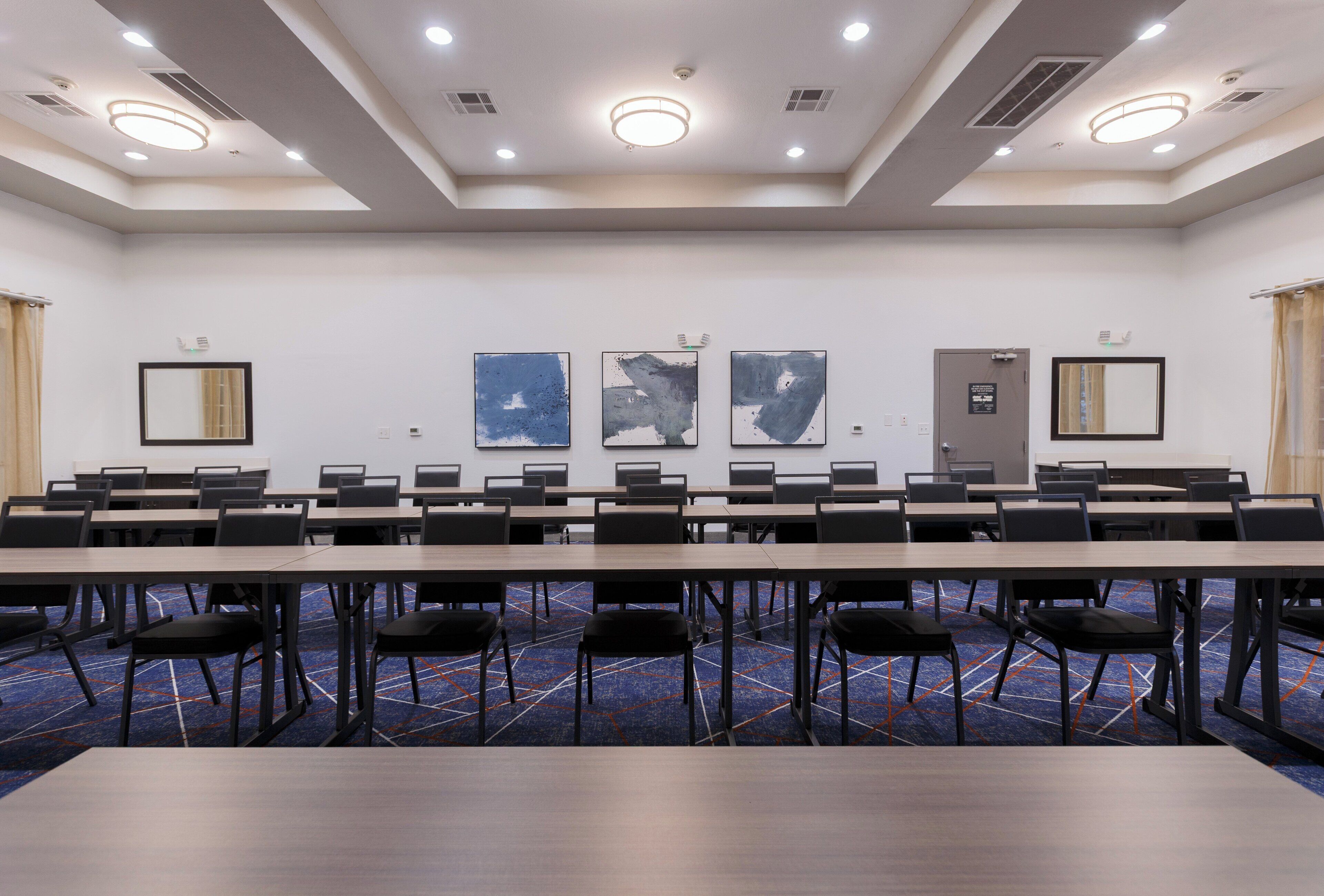 A conference room with multiple tables and chairs, a blue patterned carpet, and three abstract paintings on the wall.