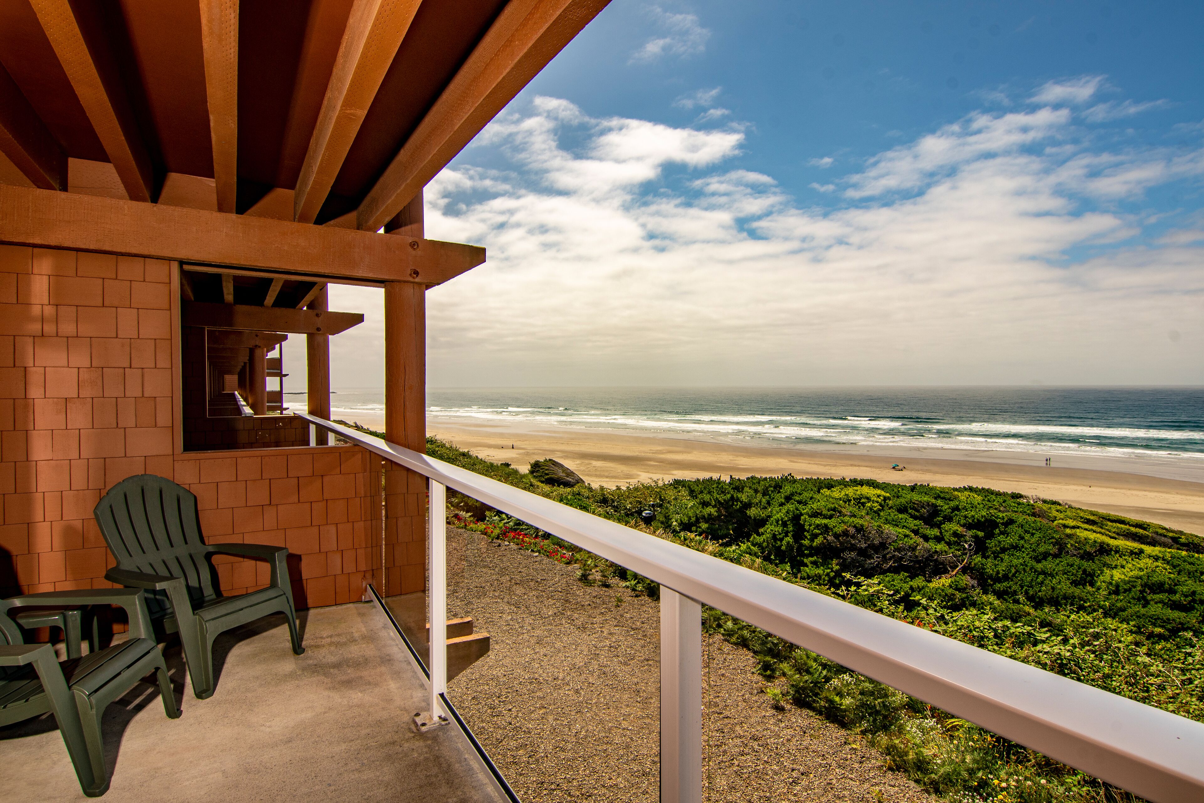 A balcony with a view of the beach, a brick wall, and two Adirondack chairs.