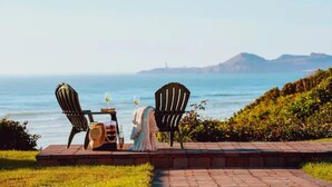 A seaside terrace with two Adirondack chairs, a table with a bottle and glass, and a dress draped over a chair. - Hallmark Resort - Newport (Newport)