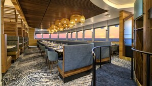A restaurant with a long table, booths, and a view of the sunset. - Hallmark Resort - Newport (Newport)