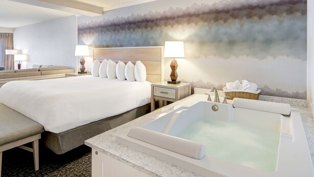 A hotel room with a large bed, a sitting area, a bathroom with a bathtub, and a wall mural. - Hallmark Resort - Newport (Newport)