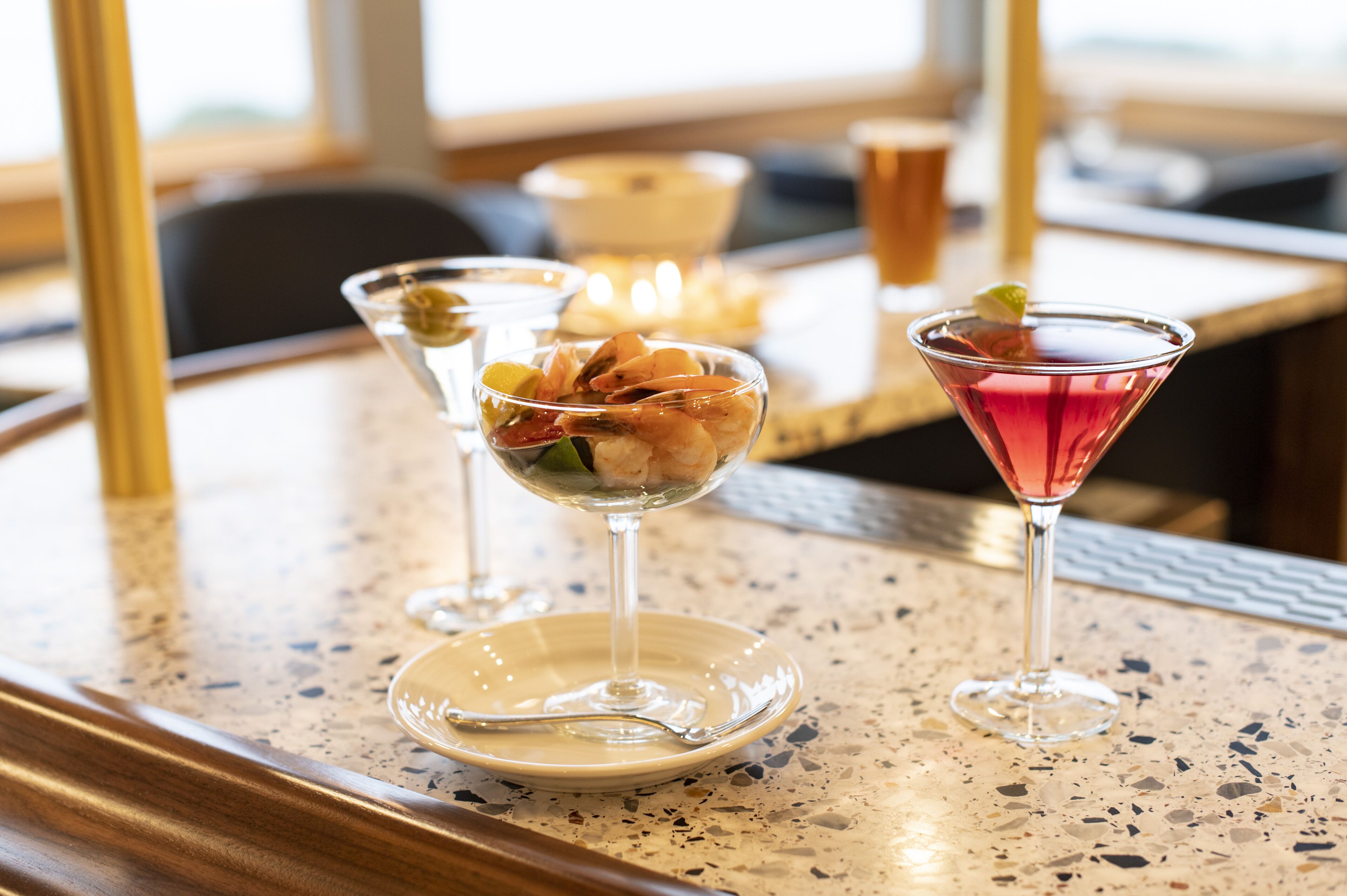 Eine Bar mit einem Barbereich, zwei Martini-Gläsern, eines mit Garnelen-Cocktail und das andere mit einem rosa Getränk.